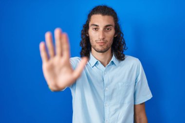 Mavi arka planda dikilen İspanyol genç adam avucunun içinde şarkı söylemeyi kesiyor. Yüzünde olumsuz ve ciddi bir jest olan uyarı ifadesi. 