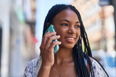 Afro-Amerikalı kadın gülümsüyor. Akıllı telefondan konuşuyor.