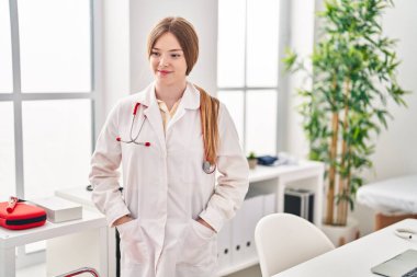 Klinikte doktor üniforması giyen genç sarışın kadın.