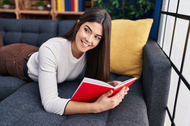 Evdeki kanepede uzanmış kitap okuyan güzel İspanyol kadın.