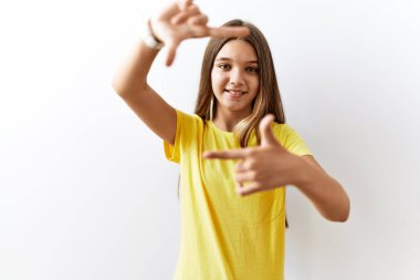 Genç esmer kız izole edilmiş arka planda yan yana duruyor gülümsüyor ve elleri ve parmakları gülen yüzlü bir çerçeve yapıyor. yaratıcılık ve fotoğrafçılık kavramı. 