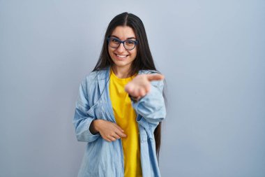 Mavi arka planda duran genç İspanyol kadın mutlu bir şekilde gülümseyerek yardım eli uzatıyor ve kabul ediyor.. 