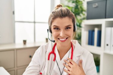 Young blonde woman wearing doctor uniform having teleconsultation at clinic