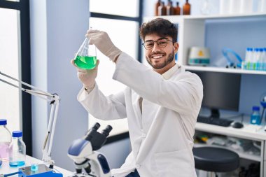 Young hispanic man scientist smiling confident measuring liquid at laboratory