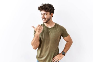 İzole edilmiş beyaz arka planda duran İspanyol bir adam gülümseyen bir yüzle yan tarafa bakıyor ve başparmağıyla işaret ediyor.. 
