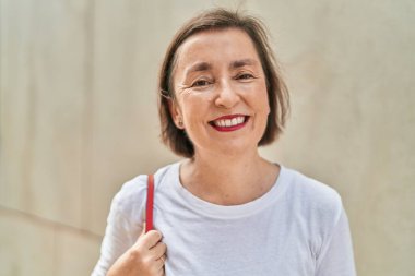 Orta yaşlı bir kadın sokakta kendine güvenerek gülümsüyor.