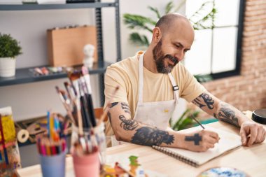 Sanat stüdyosunda kendine güvenen genç, kel bir sanatçı çizim yapıyor.