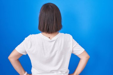 Orta yaşlı İspanyol bir kadın mavi arka planda dikiliyor geriye bakıyor kolları vücudunda. 