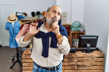 Dükkanda elinde alışveriş poşetleri tutan yakışıklı bir adam çenesi üzerinde soru sormayı düşünüyor, düşünceli bir ifade. Düşünceli bir yüzle gülümsüyor. şüphe kavramı. 