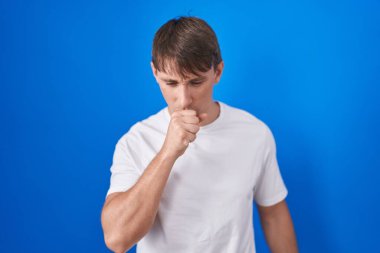 Caucasian blond man standing over blue background feeling unwell and coughing as symptom for cold or bronchitis. health care concept. 