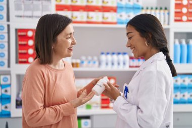 Two women pharmacist and customer holding pills bottle at pharmacy