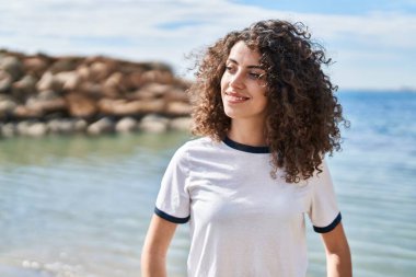 Young hispanic woman smiling confident looking to the side at seaside