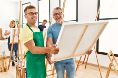 Group of middle age people drawing at art studio. Two students smiling happy holding canvas.