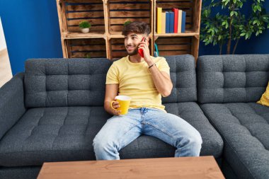 Genç Arap adam kahve içiyor ve evde akıllı telefondan konuşuyor.