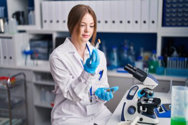 Young caucasian woman scientist smiling confident holding pill with tweezer at laboratory