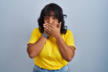 Mavi arka planda dikilen İspanyol kadın yanlışlıkla ağızlarını kapatarak şok geçirdi. gizli kavram. 