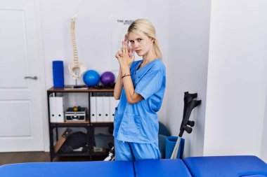 Ağrı kesici kliniğinde çalışan genç bir fizyoterapist kadın sembolik bir silahla el hareketi yapıyor, cinayet silahlarıyla oynuyor, sinirli bir yüz ifadesi var. 