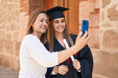 Two women mother and graduated daughter making selfie by smartphone at campus university