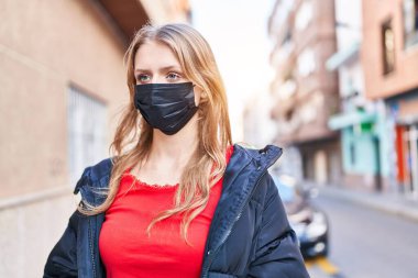 Young blonde woman wearing medical mask standing at street