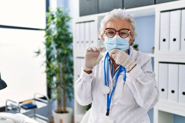 Gri saçlı, doktor üniforması giyen, tıbbi maske takan, elinde şırıngayla ciddi bir yüz ifadesi olan, eli çenesinde soru soran, kafa karıştırıcı fikirleri olan yaşlı bir kadın. 