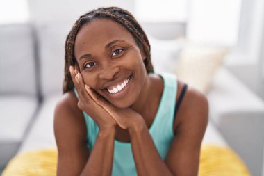 Afro-amerikalı bir kadın evdeki koltukta kendinden emin bir şekilde oturuyor.