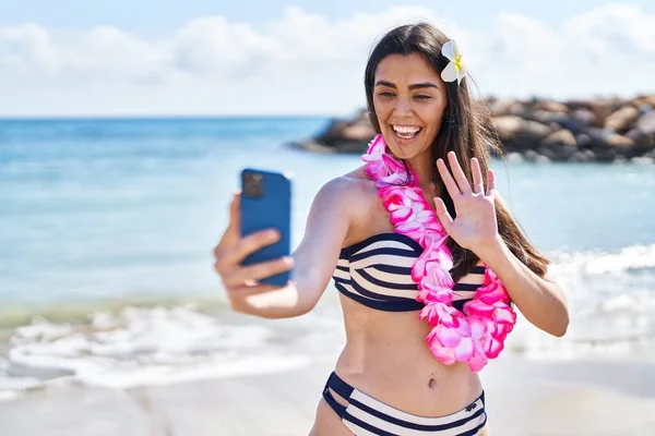 Bikini giyen genç İspanyol kadın deniz kenarında akıllı telefonla selfie çekiyor.