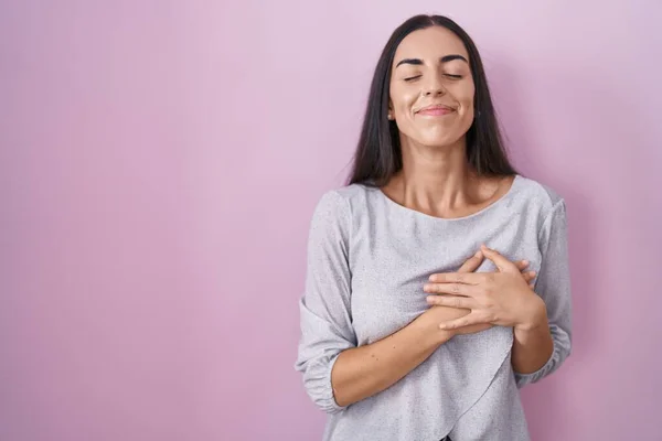 Mladá Brunetka Stojí Nad Růžovým Pozadím Usmívá Rukama Prsou Zavřenýma — Stock fotografie