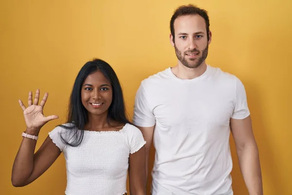 Interracial Couple Standing Yellow Background Showing Pointing Fingers Number Five — 图库照片