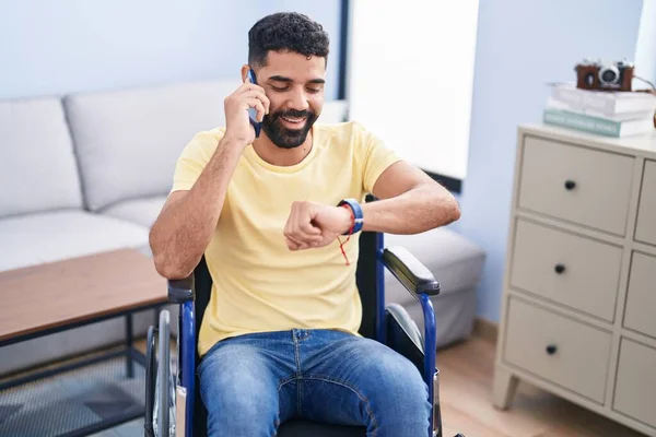 Young Arab Man Talking Smartphone Looking Watch Sitting Wheelchair Home — ストック写真