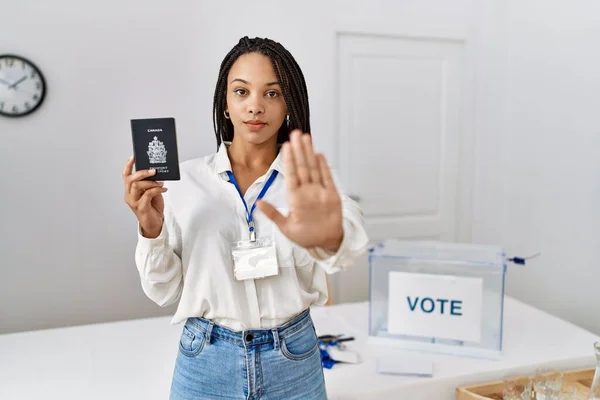 Young african american woman at political campaign election holding canada passport with open hand doing stop sign with serious and confident expression, defense gesture