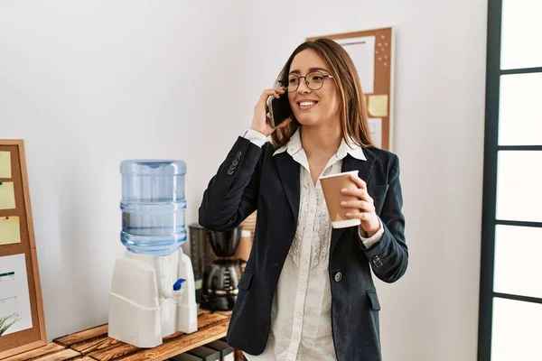 若いヒスパニック系女性のビジネスワーカーがスマートフォンで話してオフィスでコーヒーを飲む — ストック写真