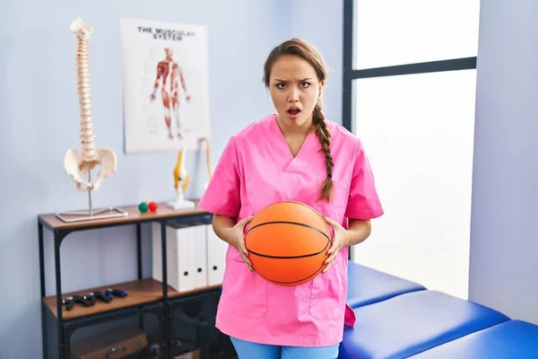 Młoda Latynoska Kobieta Pracująca Klinice Fizjoterapii Trzymająca Piłkę Kosza Szokującej — Zdjęcie stockowe