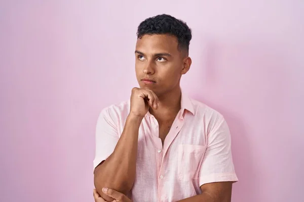 若いヒスパニック系の男性のピンクの背景の上に手をあごの質問については 集中的な表現を考えて立っている 思慮深い顔で笑顔 疑わしい概念 — ストック写真