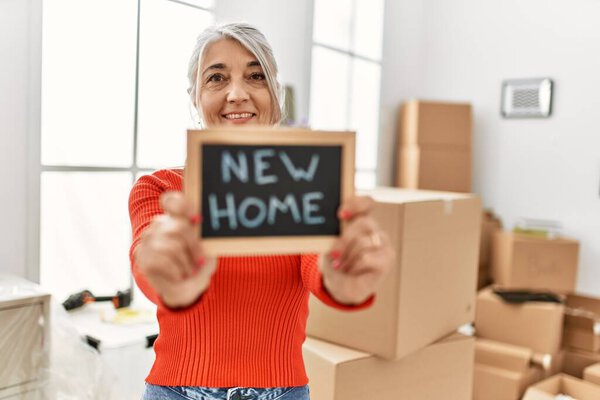 Middle age grey-haired woman smiling confident holding new home blackboard at new home
