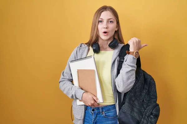 Young Caucasian Woman Wearing Student Backpack Holding Books Surprised Pointing — Stockfoto