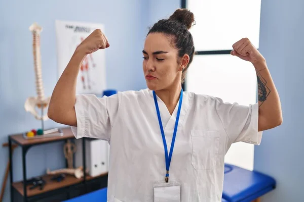 Young Hispanic Woman Working Rehabilitation Clinic Showing Arms Muscles Smiling —  Fotos de Stock