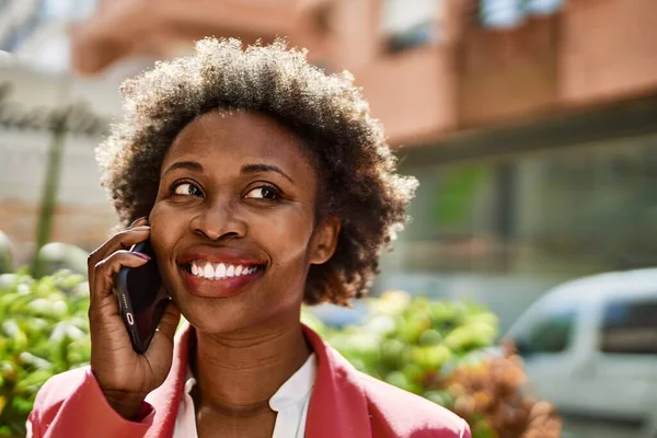 Beautiful business african american woman with afro hair smiling happy and confident outdoors at the city having a conversation speaking on the phone