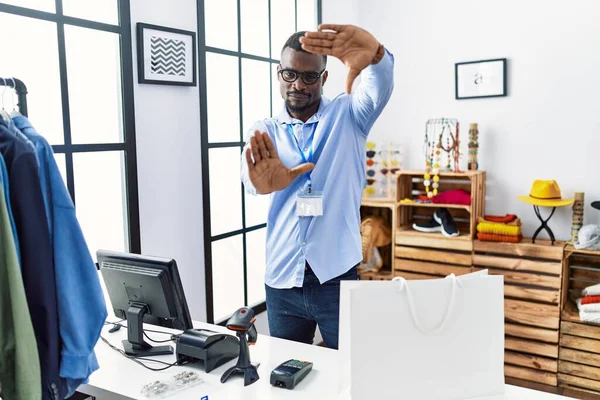 Young african man working as manager at retail boutique doing frame using hands palms and fingers, camera perspective