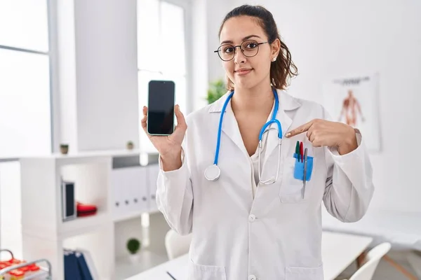 Young Hispanic Doctor Woman Holding Smartphone Showing Screen Pointing Finger — Stock Photo, Image