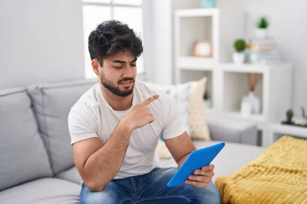 Hispanic Man Beard Using Touchpad Sitting Sofa Pointing Aside Worried — Stock Photo, Image