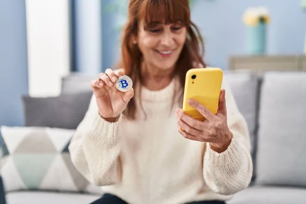 Middle Age Woman Using Smartphone Holding Bitcoin Home — Zdjęcie stockowe