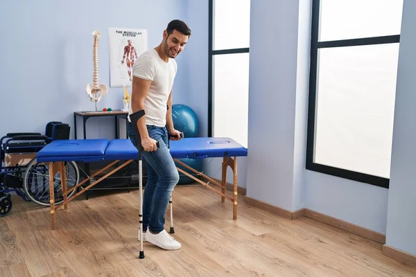 Young Hispanic Man Injured Physiotherapy Patient Using Crutches Walking Rehab — Stockfoto