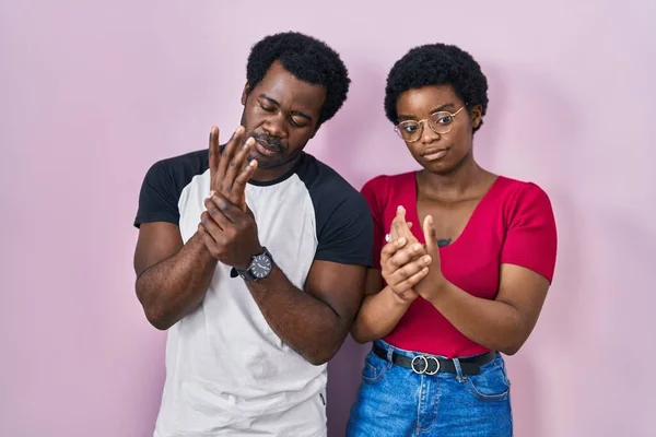 年轻的非洲裔美国夫妇站在粉色背景上 手指头疼痛 关节炎发炎 — 图库照片