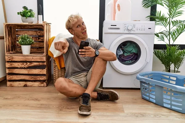 Young Blond Man Doing Laundry Using Smartphone Pointing You Camera — Stok fotoğraf
