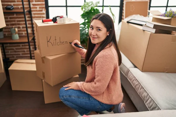 Young Hispanic Woman Writing Kitchen Word Cardboard Box New Home — 스톡 사진