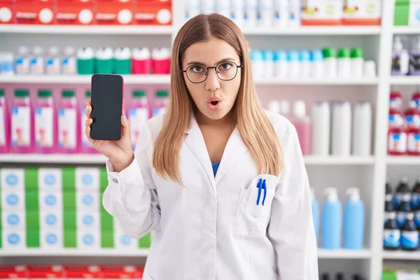 Young Blonde Woman Working Pharmacy Drugstore Showing Smartphone Screen Scared — Zdjęcie stockowe