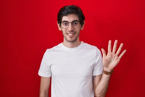 Молодой Латиноамериканец Стоит Красном Фоне Показывает Пальцами Номер Пять Улыбаясь — стоковое фото