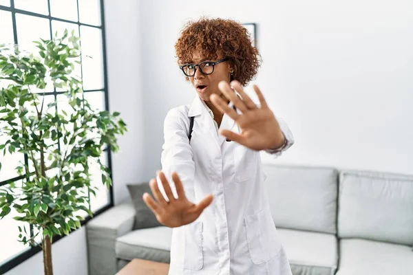 身穿医生制服和听诊器的年轻的非洲裔美国妇女害怕 表情恐惧 双手停止手势 震惊地大叫 恐慌概念 — 图库照片