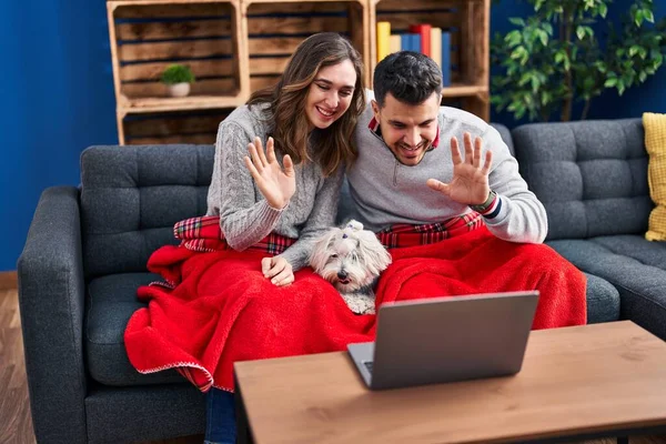 Man and woman having video call sitting on sofa with dog at home