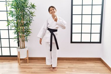 Karate kimonosu ve siyah kuşak giyen genç İspanyol kız mutlu bir el hareketi yapıyor. Kameraya bakıp başarıyı gösteren ifade. 